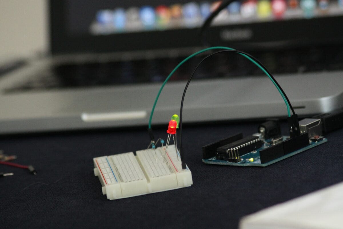 Foto de um Arduino conectado à dois leds em uma placa de prototipação e um macbook pro desfocado ao fundo
